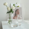 A clear glass vase holds white roses and is displayed next to smaller glass vessels.