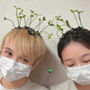 Two people wearing white face masks with bean sprout hair clips featuring small green grass tops