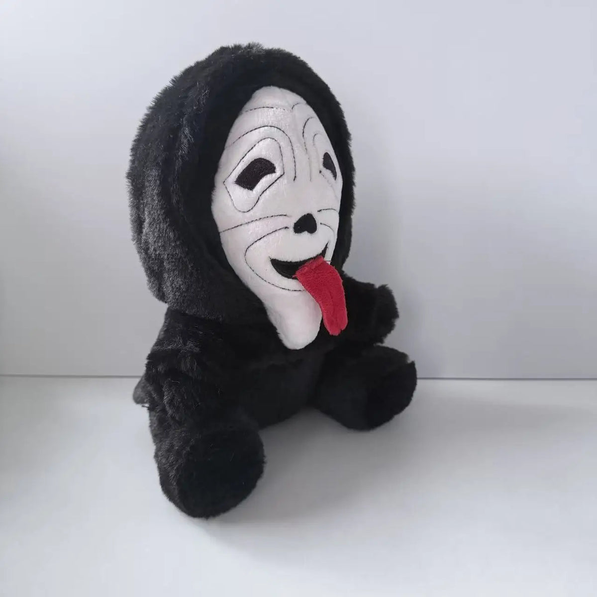 A black plush toy resembling Ghost Face with white facial markings and a red tongue.