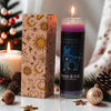 A glass candle in a rectangular box featuring a Taurus zodiac theme, set among pine branches and decorative ornaments.