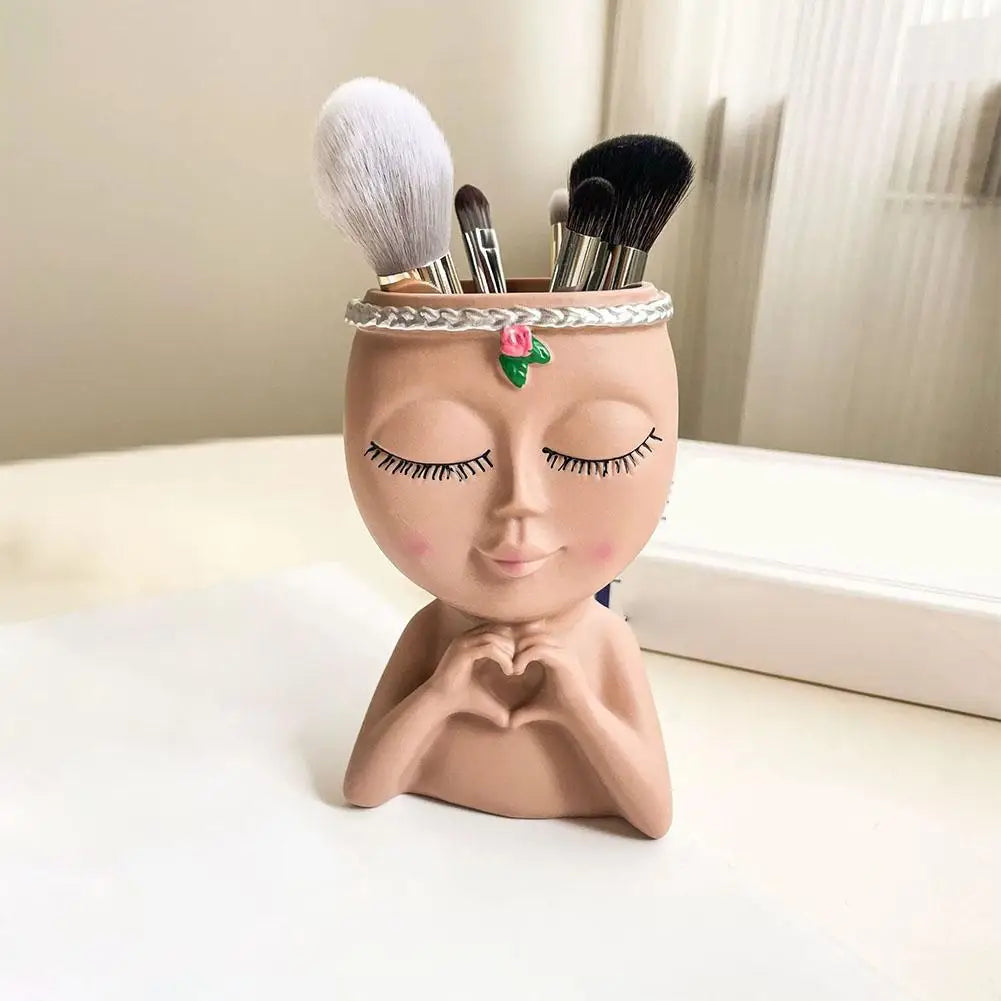 A terracotta resin girl face planter featuring closed eyes, delicate lashes, and a brush-top applicator for cosmetic use.