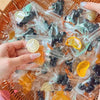 A hand holds a collection of handmade fruit keychains in clear plastic bags on a woven tray.
