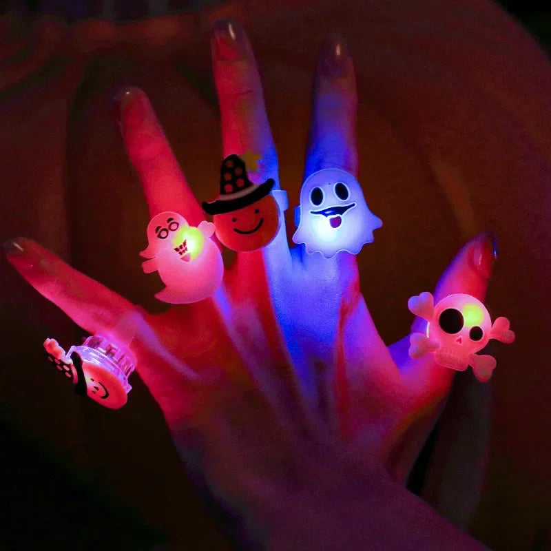 A hand holds several glowing Halloween-themed light-up rings, including a witch hat and a ghost face.