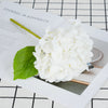 A close-up photo of a white artificial hydrangea flower cluster resting on a piece of paper with text.