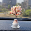 A small tree ornament with pink and white simulated flowers sits on a white ceramic base.