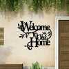 A black metal script sign welcoming visitors to a home mounted on an exterior wall.