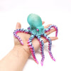 A hand holds a teal and purple articulated 3D printed octopus figurine with eight tentacles.