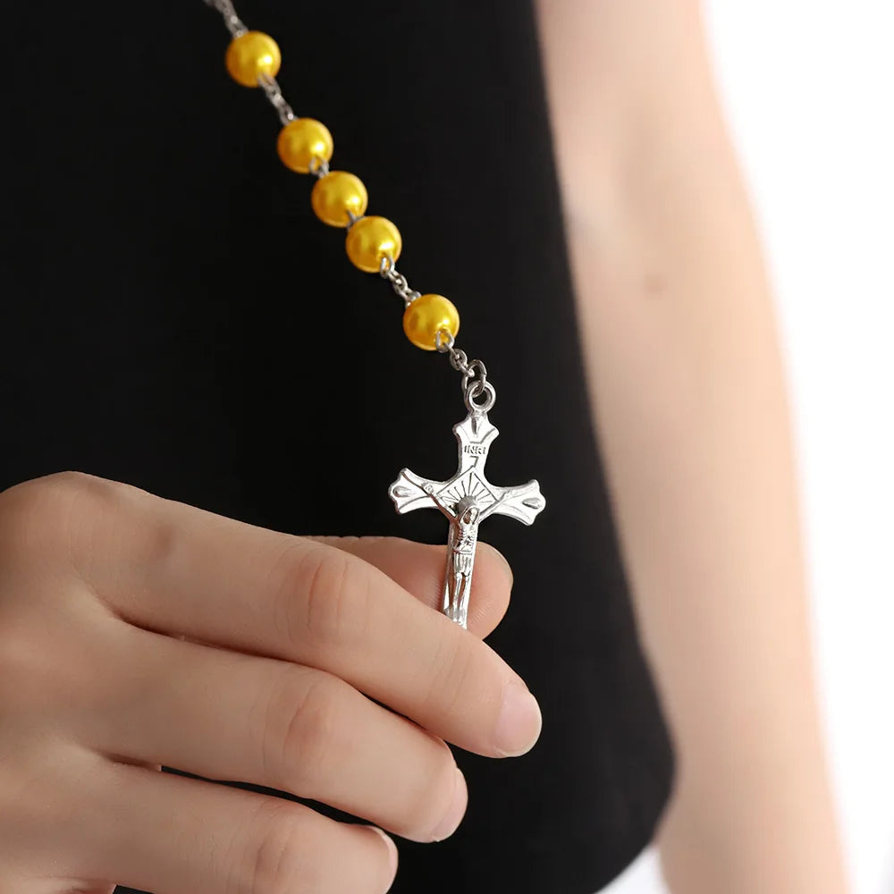 A hand holds a vintage cross and Virgin Mary pendant rosary necklace with gold beads.