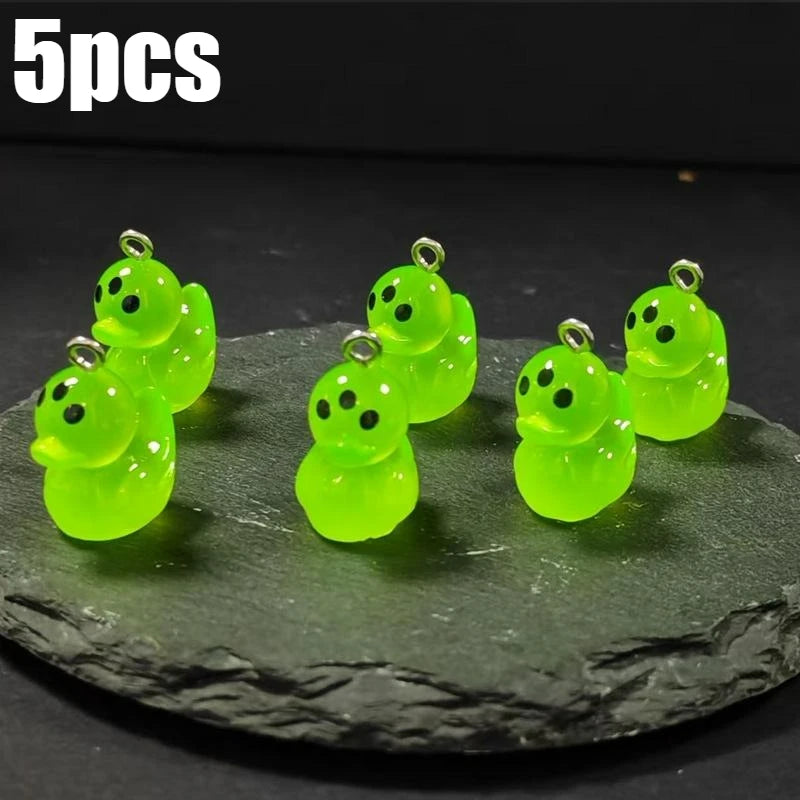 Five glow-in-the-dark green cartoon alien kitty duck resin charms displayed on a dark surface.