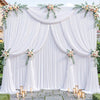 A white fabric backdrop with draped curtains and floral greenery for an event setting.