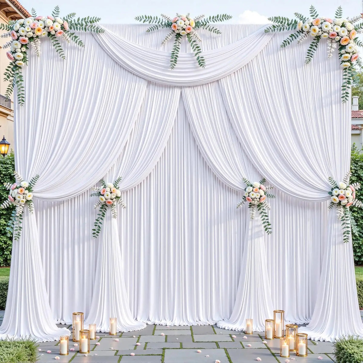 A white fabric backdrop with draped curtains and floral greenery for an event setting.