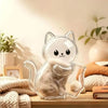 A clear capsule cat whisker keepsake magnet sitting on a wooden surface next to soft textiles and a potted plant.