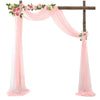 A wooden cross decorated with pink floral garlands and draped with sheer pink chiffon fabric panels.