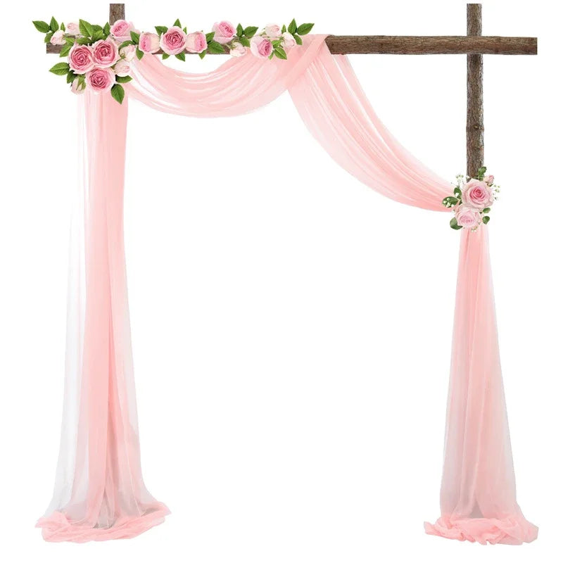 A wooden cross decorated with pink floral garlands and draped with sheer pink chiffon fabric panels.