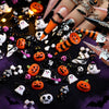 A variety pack of black and orange Halloween resin nail charms, including pumpkins, bats, and ghosts, displayed on fingers.