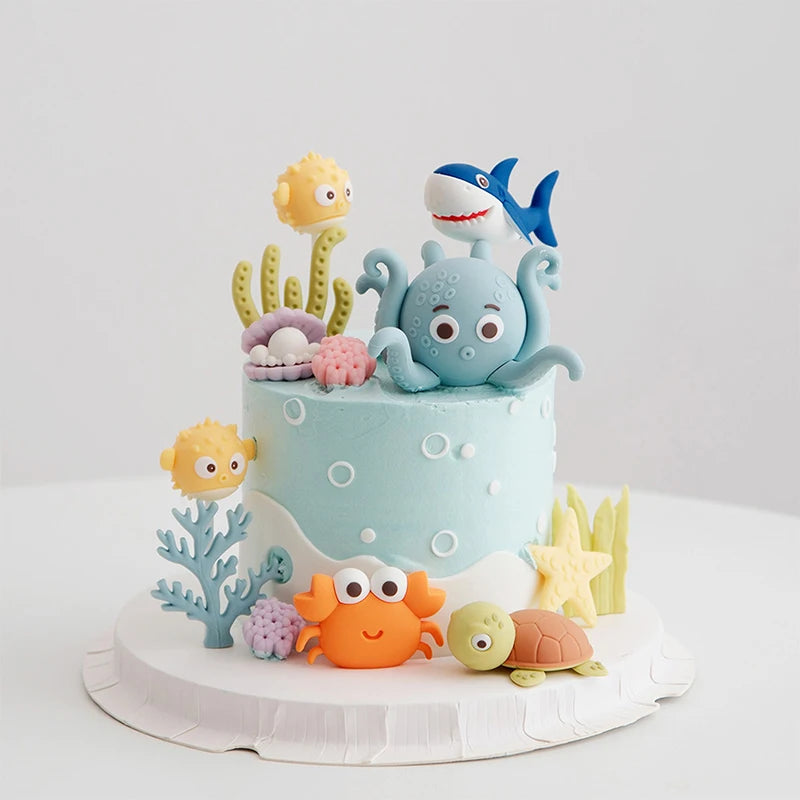 A tiered cake decorated with ocean animal toppers including a whale, octopus, and turtle.