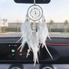 A dream catcher car pendant featuring a crystal mirror and white feathers hanging from a black car interior.