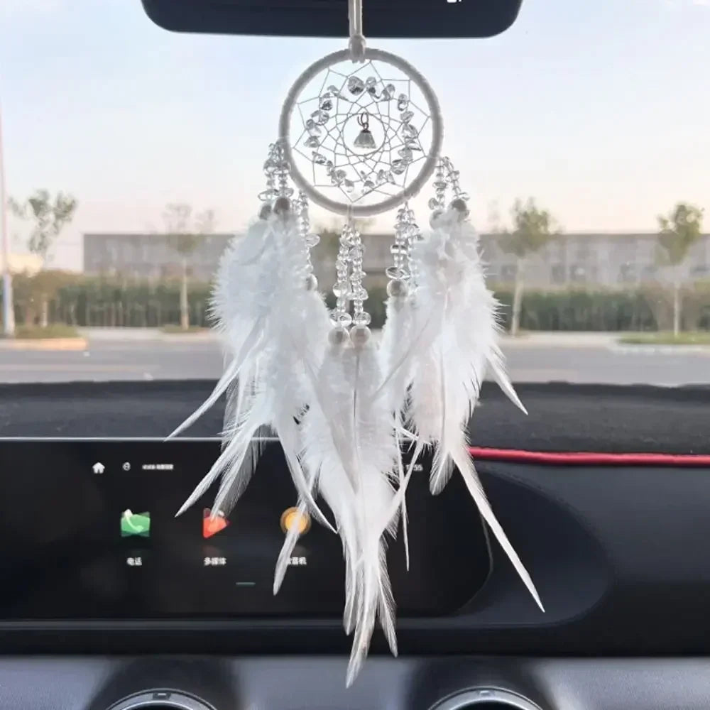 A dream catcher car pendant featuring a crystal mirror and white feathers hanging from a black car interior.