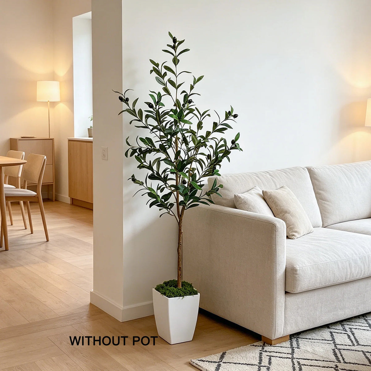 A lifelike artificial olive tree in a white planter sits next to a beige sofa in a bright, modern living room.