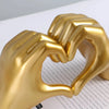 A golden resin sculpture of two hands forming a heart shape.