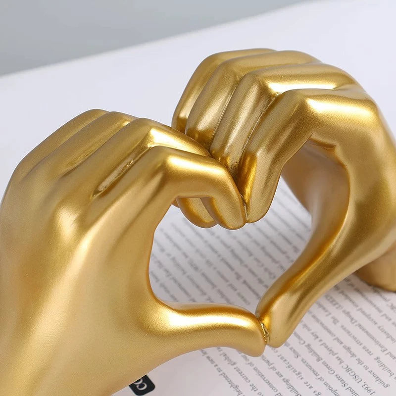 A golden resin sculpture of two hands forming a heart shape.
