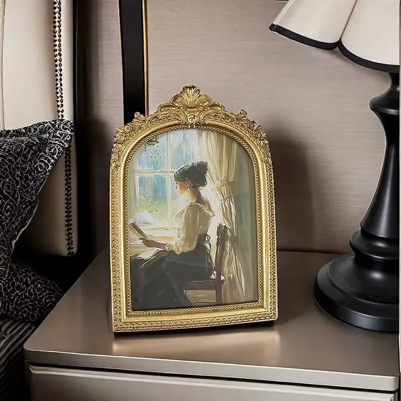 An ornate gold-framed vintage resin photo of a woman in period attire sitting and reading.