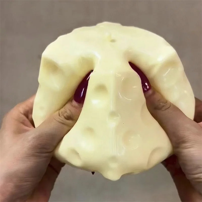 A hand holds a large, pale yellow cheese cube stress ball fidget toy against a neutral background.