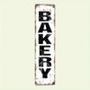 A distressed white metal sign with the word BAKERY painted in black block letters.
