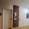 A white paneled door next to a textured brown brick wall featuring an abstract artwork.