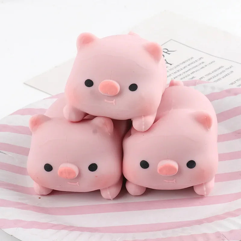Three pink pig mochi squishy stress relief toys are displayed on a striped surface.