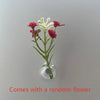 A small glass vase holds a plant with pink and white flowers on a light gray background.