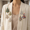 A beige blazer features several sparkling rhinestone Christmas tree brooches pinned on the lapel.
