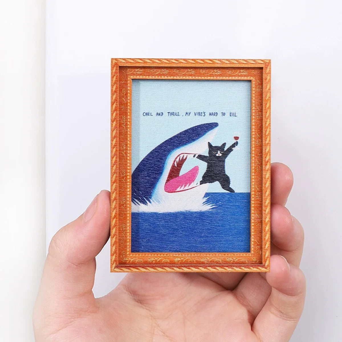 A framed artwork featuring a silhouette of a cat diving into blue water on a white background.