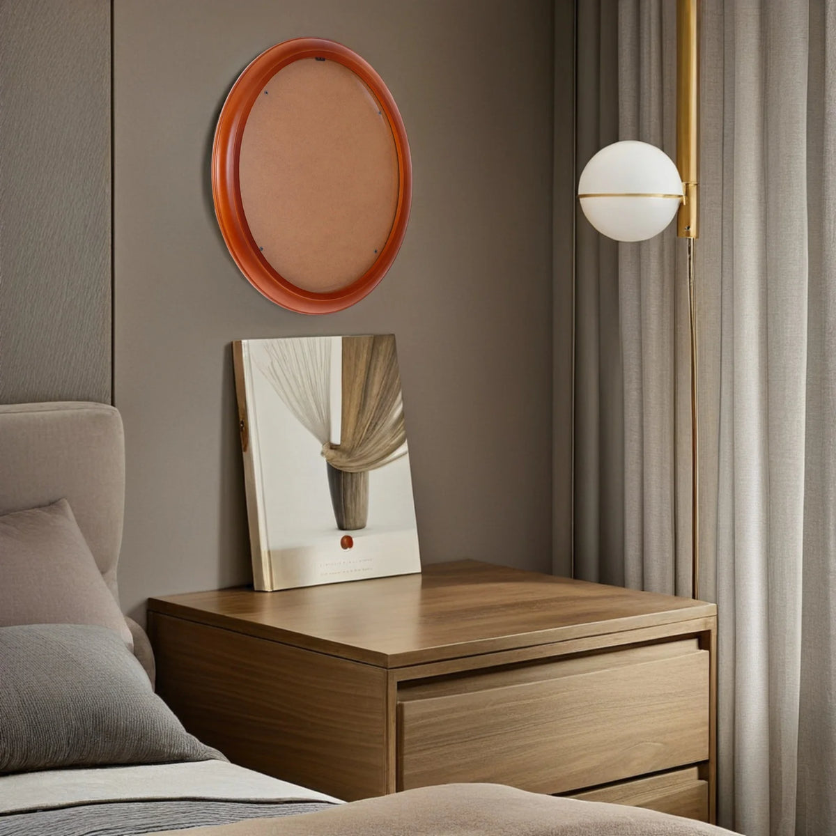 An elegant oval wooden wall photo frame hangs on a beige wall above a wooden nightstand in a softly lit room.