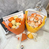 A bouquet of artificial orange and cream roses wrapped in yellow paper with a gold ribbon.
