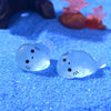 Two translucent blue glow in the dark resin sea animal figurines resting on a blue glitter surface.
