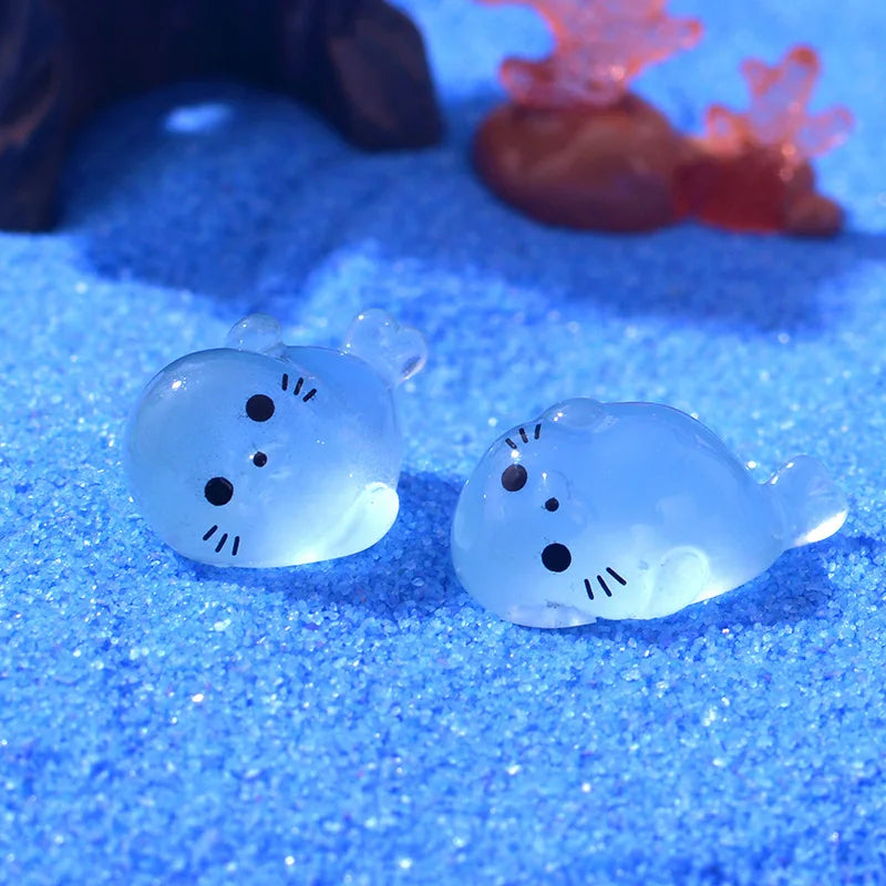 Two translucent blue glow in the dark resin sea animal figurines resting on a blue glitter surface.