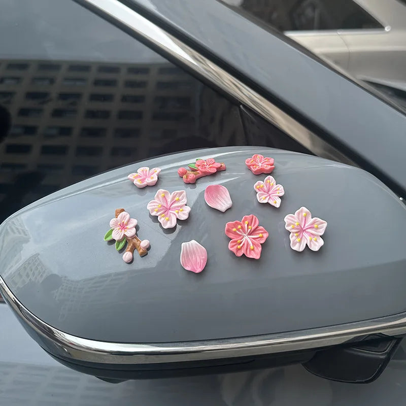A collection of pink and white 3D peach blossom ornaments displayed on a car dashboard.