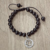 A black beaded bracelet with a silver zodiac sign charm is displayed on a wooden surface.