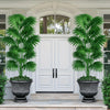 Large artificial palm trees in black pots flanking a white door on a porch.