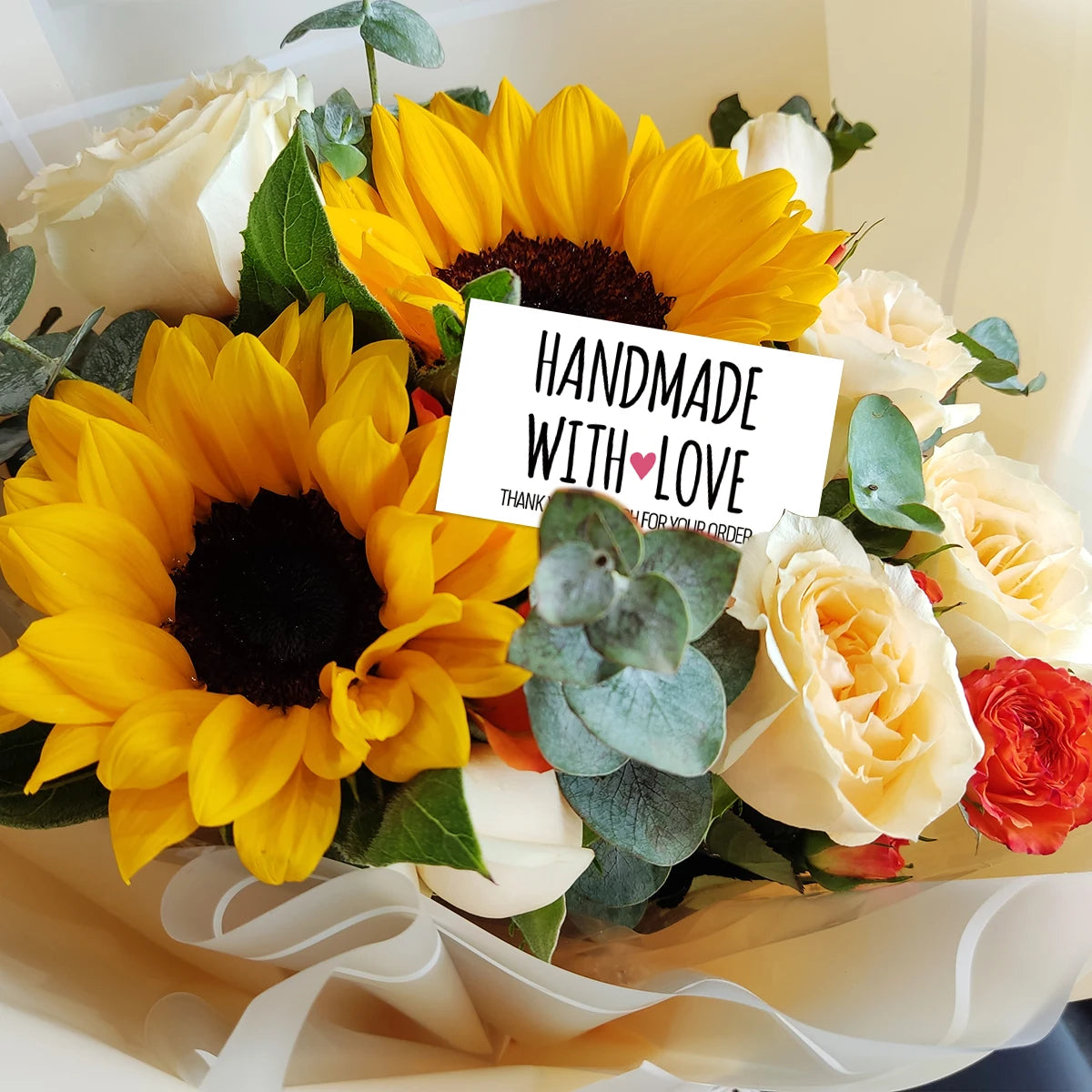 Blumenstrauß aus gelben und cremefarbenen Blumen, darunter Sonnenblumen und Rosen, mit einer handgemachten Dankeskarte.