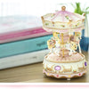 A delicate pink and cream handmade resin carousel music box with gold accents sits on a wooden surface.