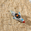 Décoration de gâteau d'astronaute miniature argentée avec des accents bleus repose sur du sable grossier.