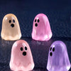 Four luminous ghost mini figurines in pastel shades of yellow, pink, and purple on a dark surface.
