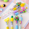 A set of five cute cartoon mini ballpoint pens in various bright colors and designs resting on a white grid paper.