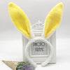 A pair of yellow bunny ears headband with a silver clip displayed in front of a white photo frame.
