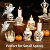 A collection of resin skull candle holders and bat decorations on a wooden surface.