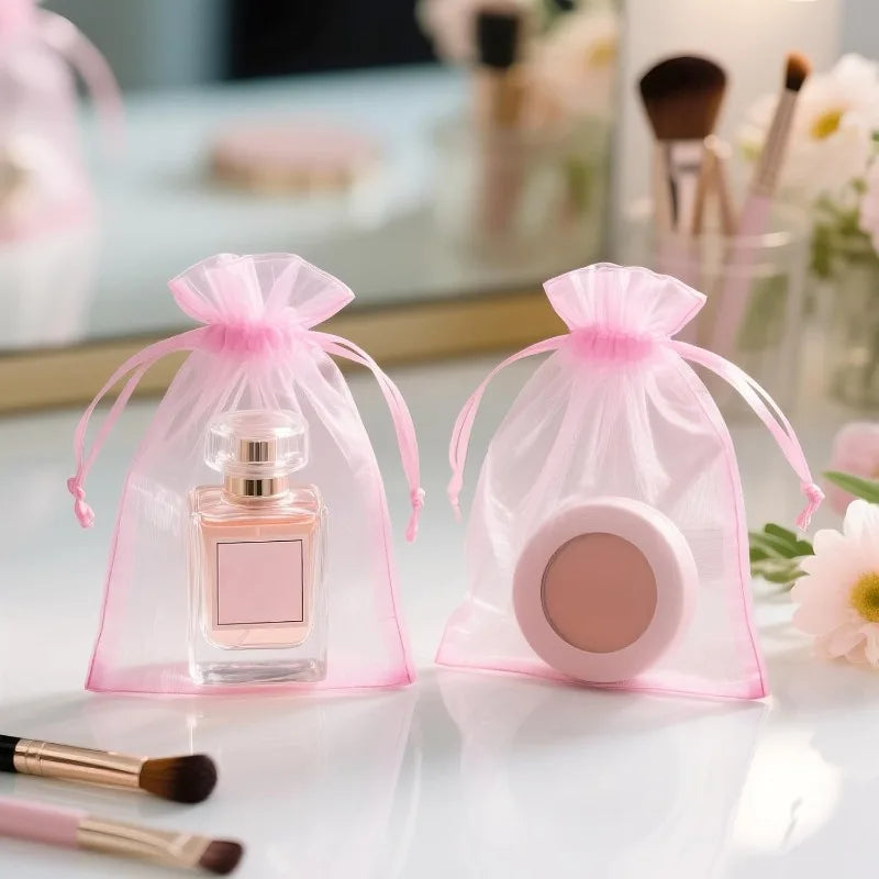 Two pink organza drawstring gift bags containing cosmetic products are displayed on a white surface.