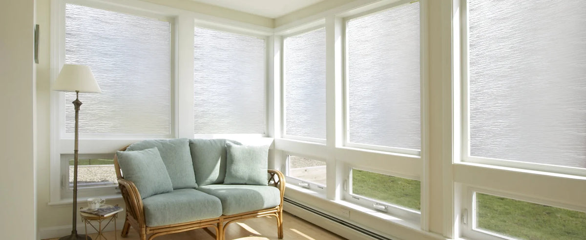 A light blue sofa is visible in a bright room with large windows covered by white frosted glass privacy film.