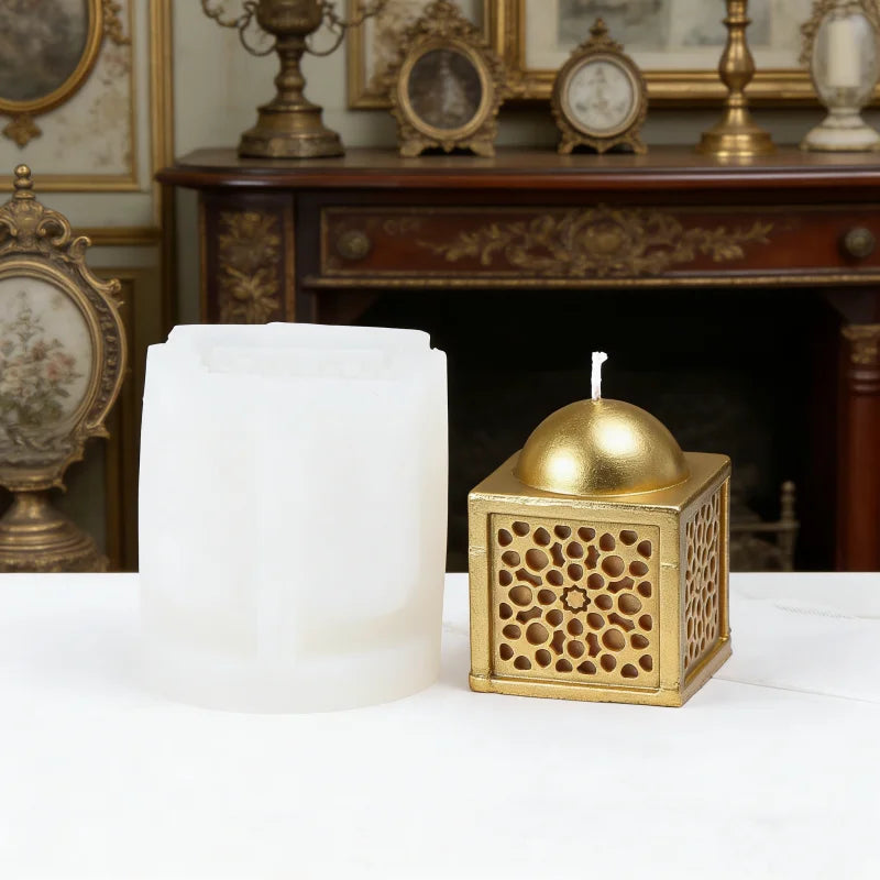 A white pillar candle and a gold patterned candle holder are displayed on a white surface.